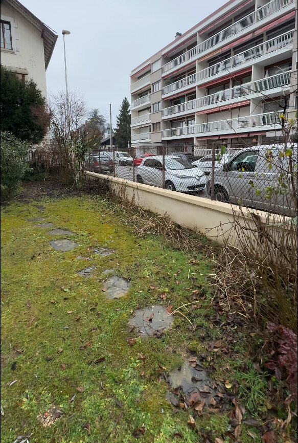 Jardin d’Annecy avant les travaux : pelouse moussue le long d’un muret, sans plantation